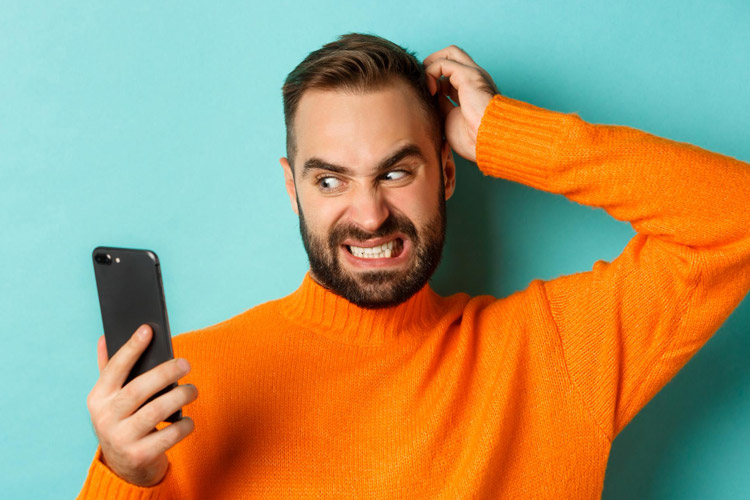 Mann schaut verunsichert ins Handy und fährt sich durchs Haar